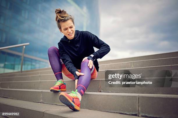 chica de la lesionados corredor está sentado en las escaleras de la ciudad - woman holding legs fotografías e imágenes de stock