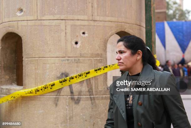 An Egyptian woman stands next to a cordoned off bullet-riddled wall at the site of a gun attack at a church south of the capital Cairo, on December...