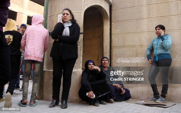 Egyptian women use their phones as they stand outside the Mar Mina Church south of the Egyptian capital Cairo following a gun attack on December 29,...