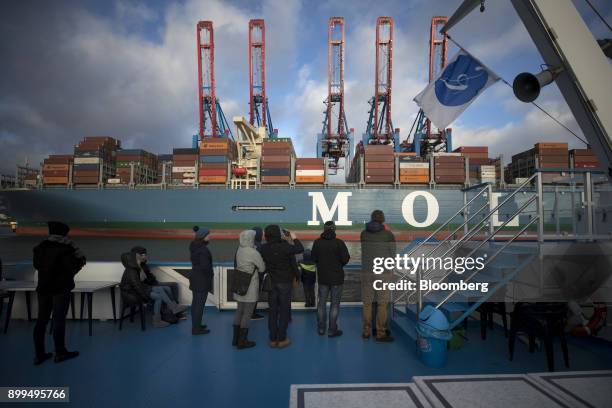 Passengers on a tourist boat look out towards the Mol Truth container vessel docked at the Hamburger Hafen und Logistik AG Container Terminal...