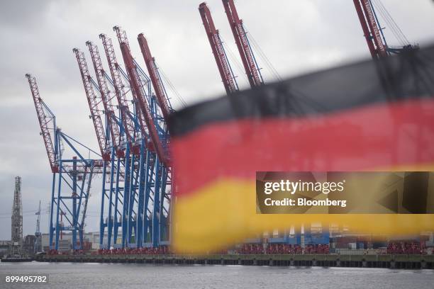 German national flag flies in front of cranes at the Hamburger Hafen und Logistik AG Container Terminal Tollerort in the Port of Hamburg in Hamburg,...