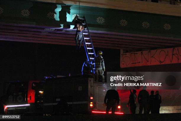 Graphic content / Firefighters and police work at a crime scene where the body of a man was found hanging from a vehicular bridge at the entrance to...