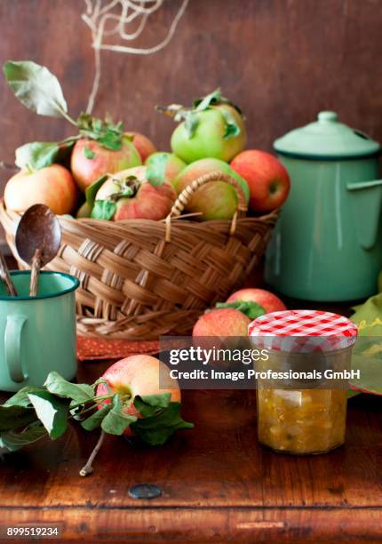 a jar of yellow tomato and apple chutney on a table with a basket of fresh apples - homemade apple sauce stock pictures, royalty-free photos & images