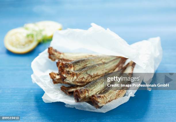 a pile of sprats on crumpled white paper on a blue surface - sprat fish stock pictures, royalty-free photos & images
