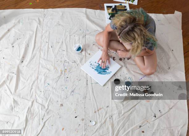 overhead view of female artist sitting on dust sheet finger painting abstract canvas - protective sheet stock pictures, royalty-free photos & images