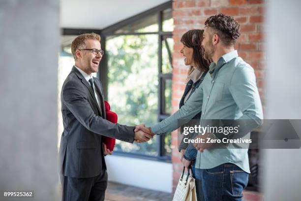 estate agent shaking hands with couple in empty home - real estate sold stock pictures, royalty-free photos & images