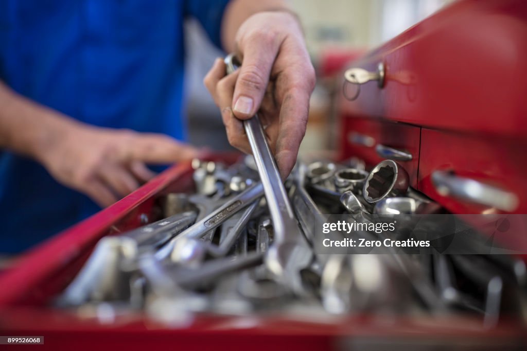 Hands of male car mechanic selecting wrench from tool box in repair garage