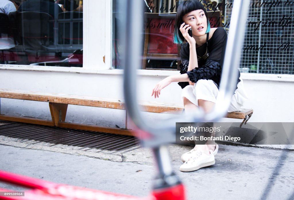 Young stylish woman sitting outside shop making smartphone call