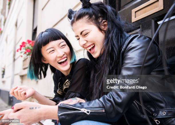 two young stylish female friends sitting doorstep laughing - chinese friends stock pictures, royalty-free photos & images