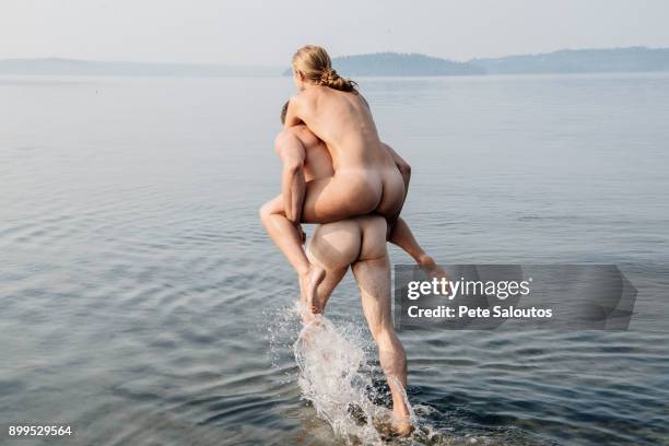 nude man giving nude woman piggyback into water - skinny dipping stock pictures, royalty-free photos & images