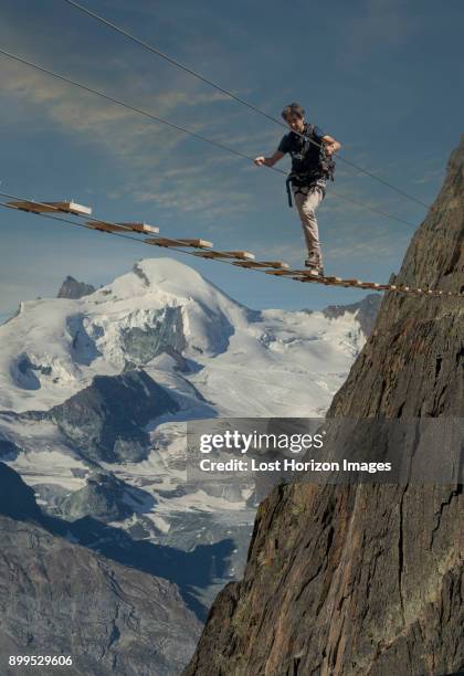 mature male climber stepping across wire rope bridge, jegihorn, valais, switzerland - touwbrug stockfoto's en -beelden