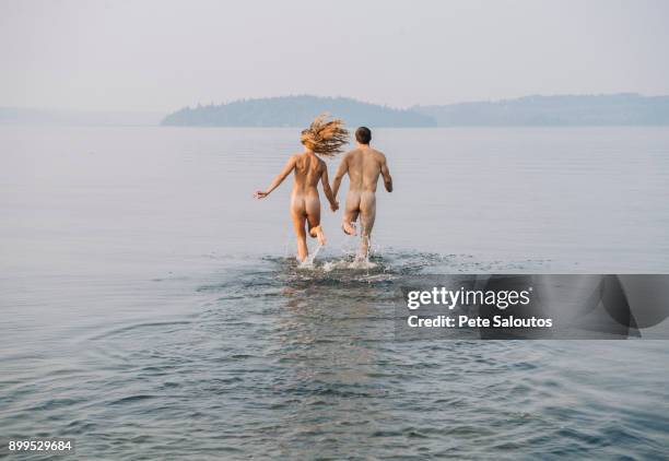 rear view of nude couple running into water - skinny dipping stock-fotos und bilder