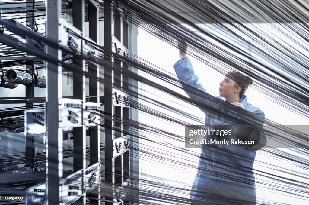 Female operator with carbon fibre thread on loom in carbon fibre production facility