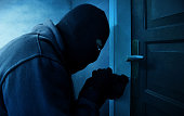 Masked thief using lock picker to open locked door