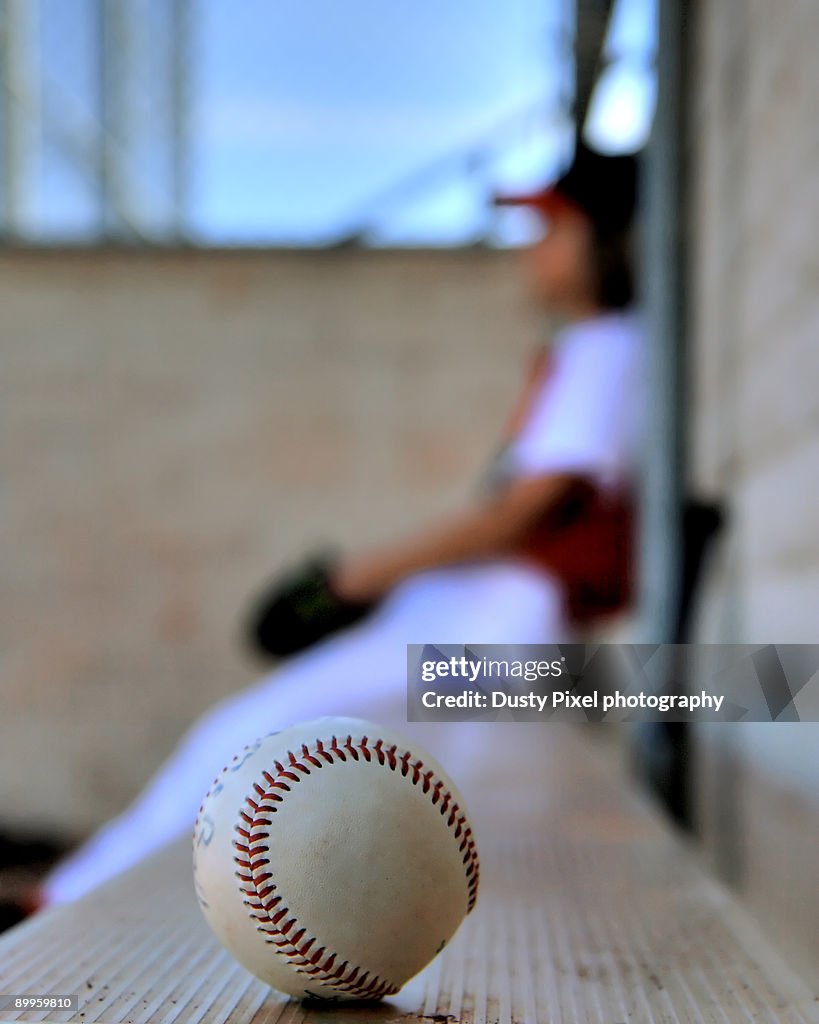 A baseball player sits on dugout bench