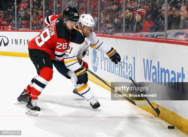 Kyle Okposo of the Buffalo Sabres attempts to move the puck around Damon Severson of the New Jersey Devils during the first period at the Prudential...