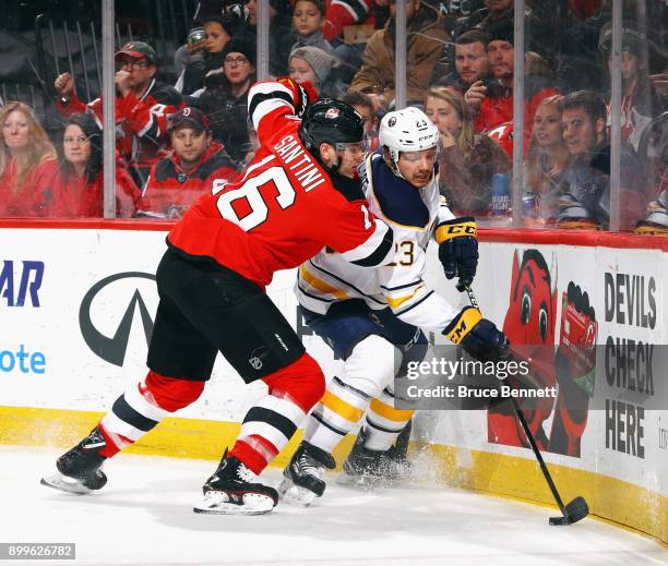 Sam Reinhart of the Buffalo Sabres is checked into the boards by Steven Santini of the New Jersey Devils during the first period at the Prudential...