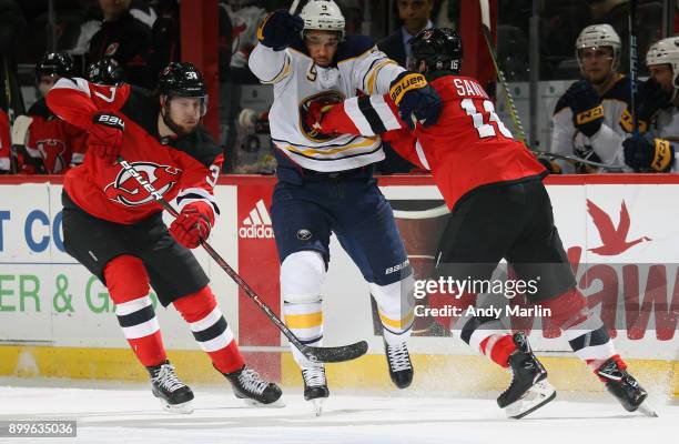 Evander Kane of the Buffalo Sabres skates between Steven Santini of the New Jersey Devils and Pavel Zacha during the game at Prudential Center on...
