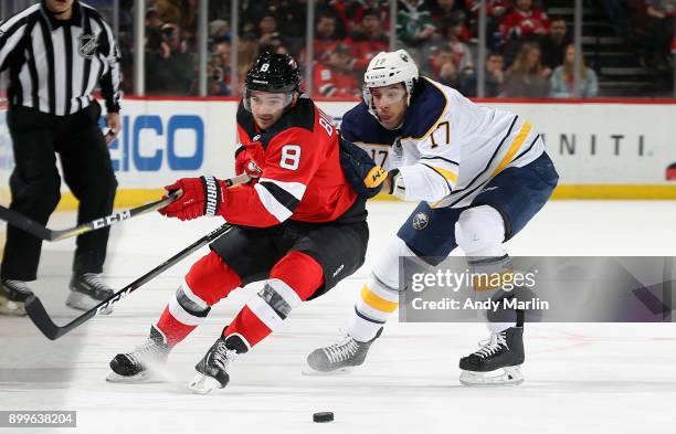 Will Butcher of the New Jersey Devils and Jordan Nolan of the Buffalo Sabres battle for a loose puck during the game at Prudential Center on December...