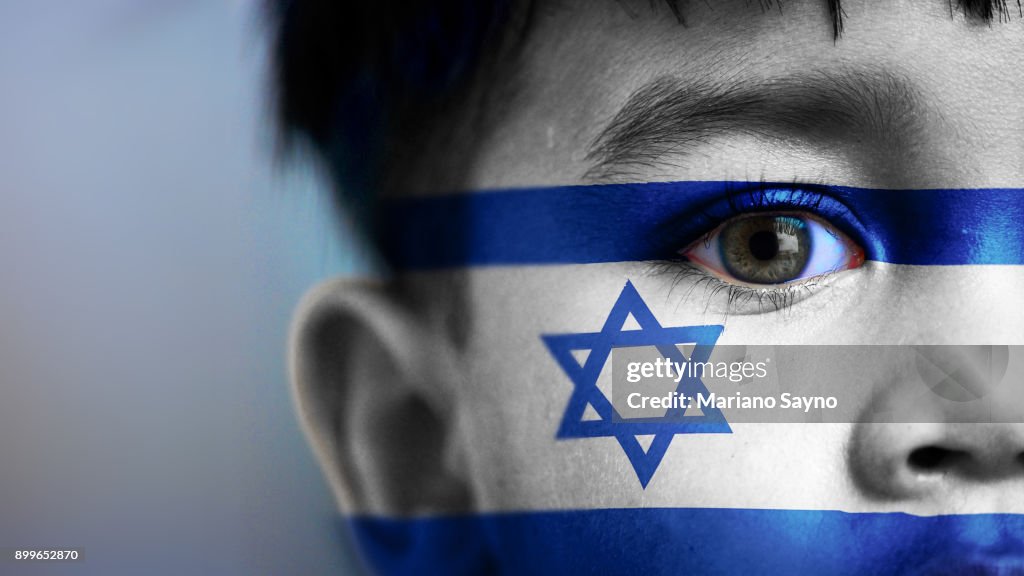 Boy's face, looking at camera, cropped view with digitally placed Israel flag on his face.