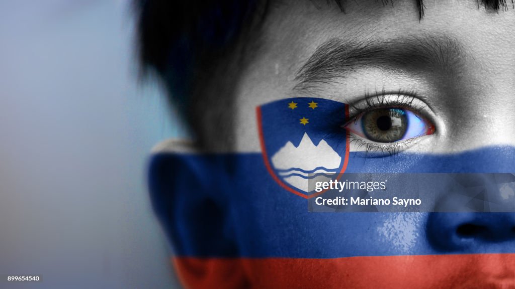 Boy's face, looking at camera, cropped view with digitally placed Slovenia flag on his face.