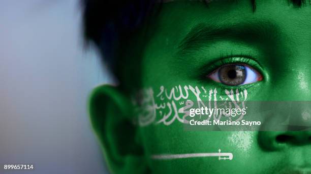 boy's face, looking at camera, cropped view with digitally placed saudi arabia flag on his face. - saudi arabian flag stockfoto's en -beelden