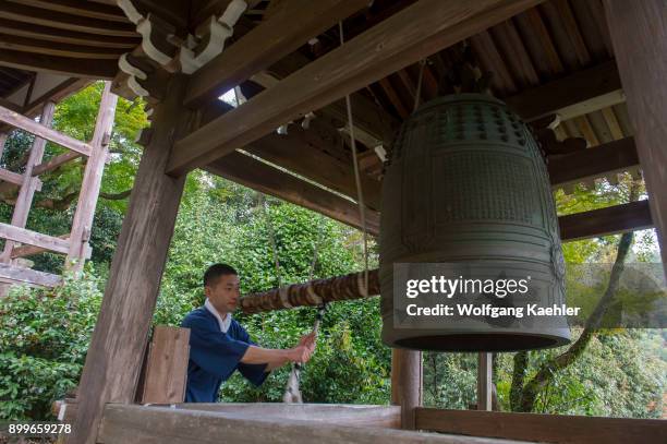 Young monk is ringing the bell at the Senkoji Temple in the forest above the Katsura River in Kyoto, Japan.