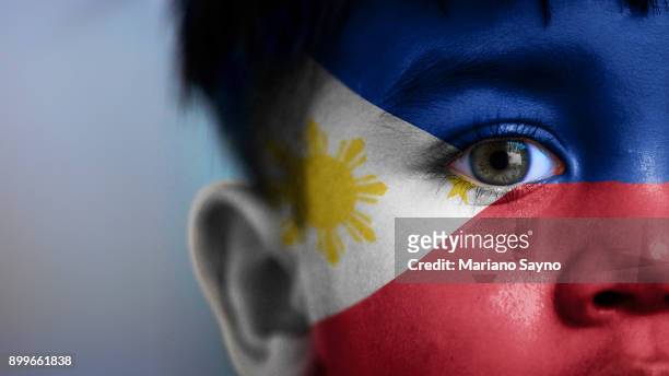 boy's face, looking at camera, cropped view with digitally placed philippines flag on his face. - philippines national flag stock-fotos und bilder