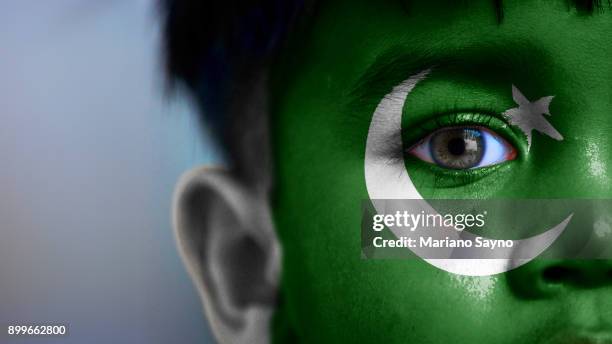 boy's face, looking at camera, cropped view with digitally placed pakistan flag on his face. - pakistani flag stock pictures, royalty-free photos & images