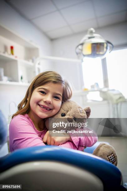 little girl holding a teddy bear in his arms at dentists office - pediatric dentistry stock pictures, royalty-free photos & images