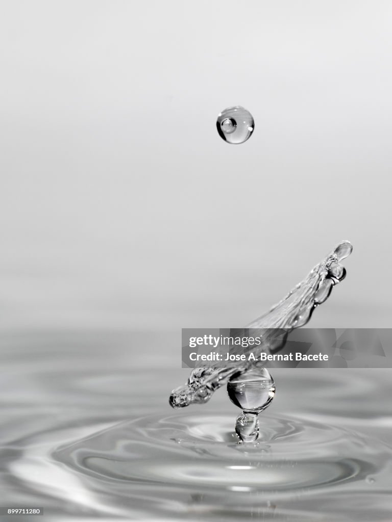 Group of drops on line suspended in the air, falling down on a water surface that forms figures and abstract forms, on a gray background