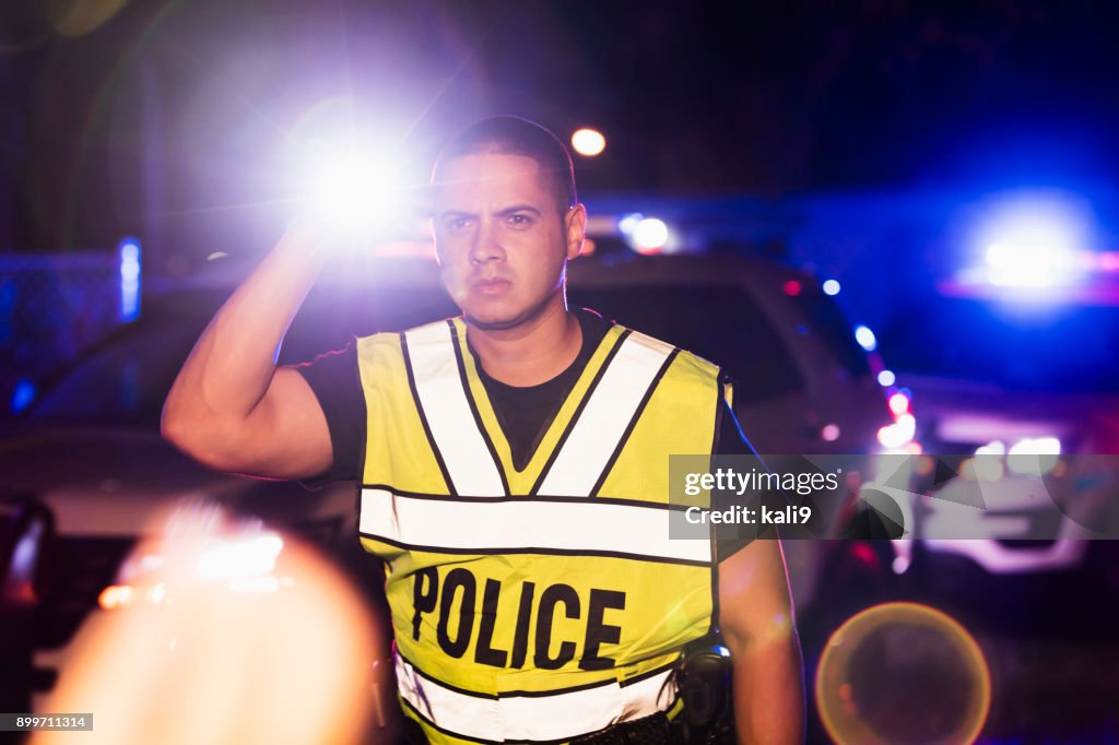 Hispanic police officer at night, flashing lights