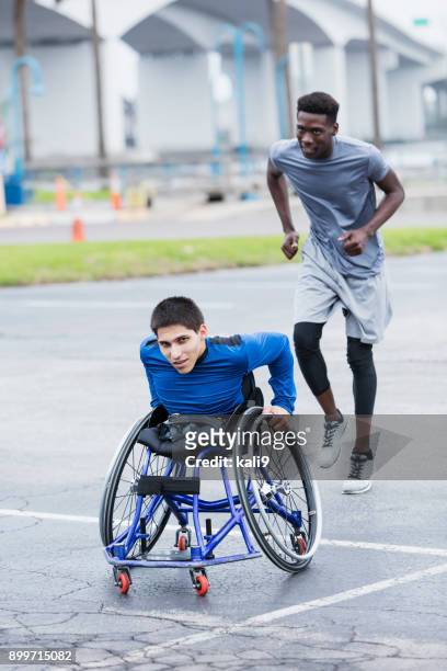determined young man in wheelchair racing, with friend - center athlete stock pictures, royalty-free photos & images