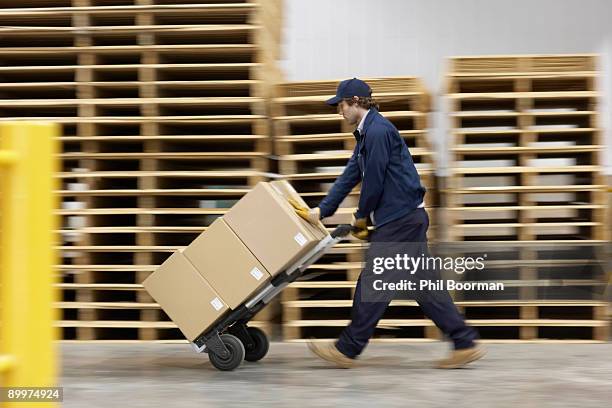 worker pushing trolley in warehouse - empujar fotografías e imágenes de stock