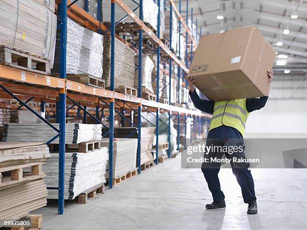 worker struggling with box in warehouse - hazardous workplace stock-fotos und bilder