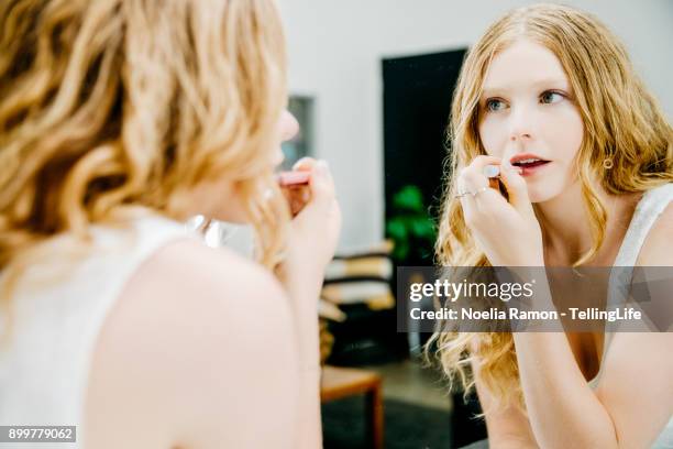 a young woman putting lipstick in front of a mirror - thin lips stock pictures, royalty-free photos & images