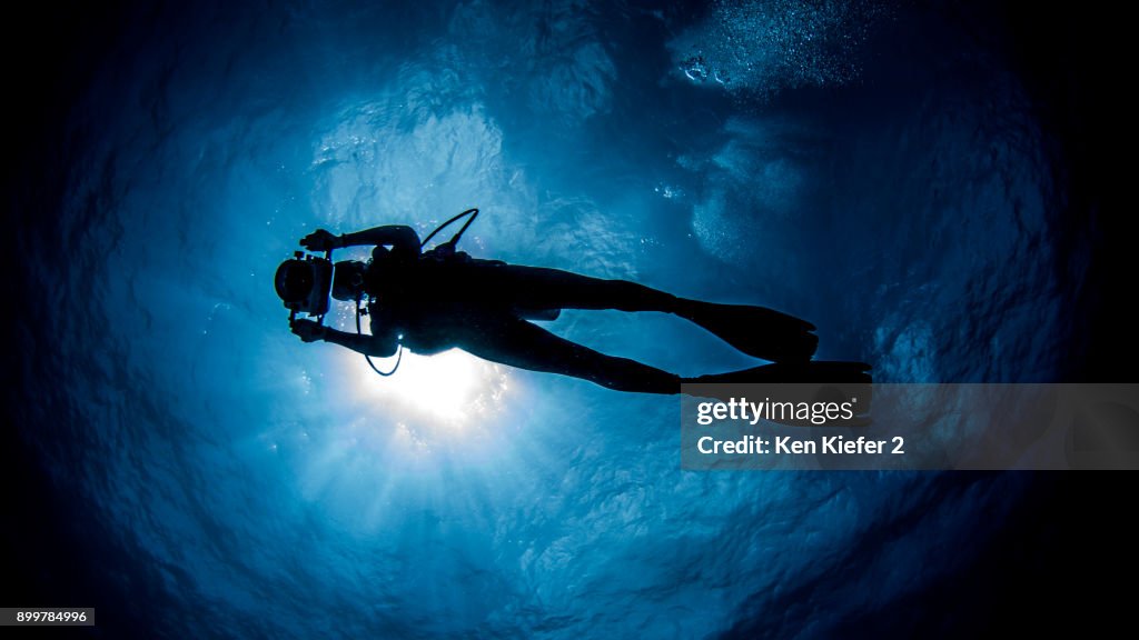 Diver with camera swimming under sunrays