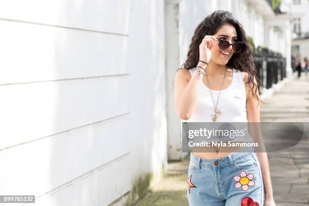 young woman with long wavy hair strolling on street looking over sunglasses - lowering stock-fotos und bilder