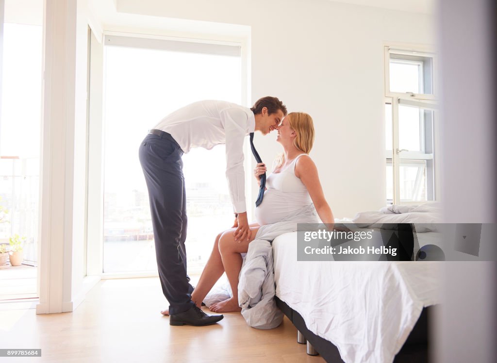 Pregnant woman pulling partners tie in bedroom