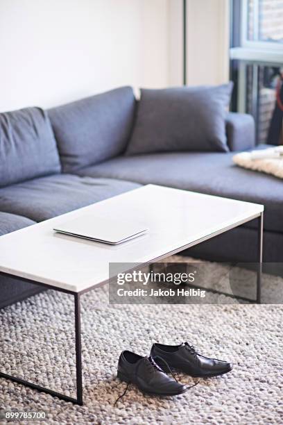 living room with laptop on coffee table and mens shoes on rug - jakob helbig stock pictures, royalty-free photos & images