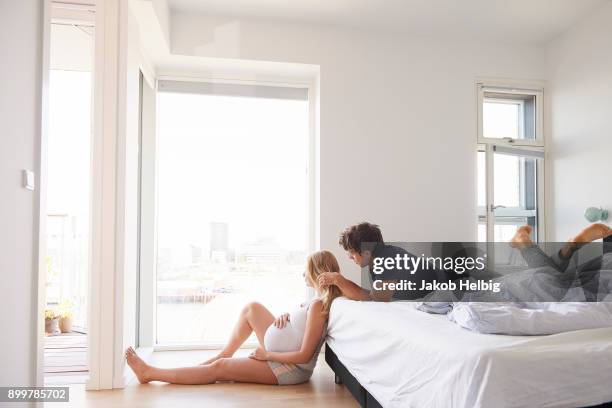 man lying on bed with hand on pregnant girlfriends hair - jakob helbig fotografías e imágenes de stock