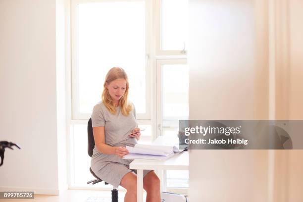 pregnant young woman at desk looking at smartphone and paperwork - jakob helbig fotografías e imágenes de stock