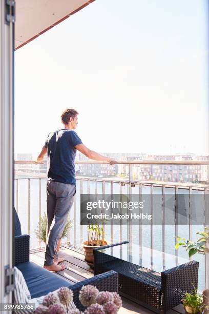 mid adult man looking out from waterfront apartment balcony - jakob helbig fotografías e imágenes de stock