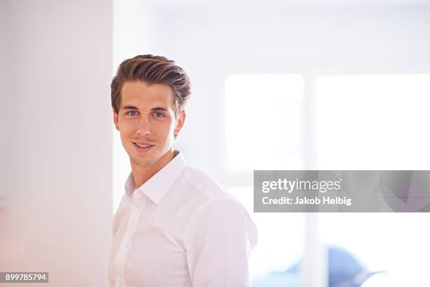 portrait of mid adult man wearing white shirt in living room - jakob helbig stock pictures, royalty-free photos & images