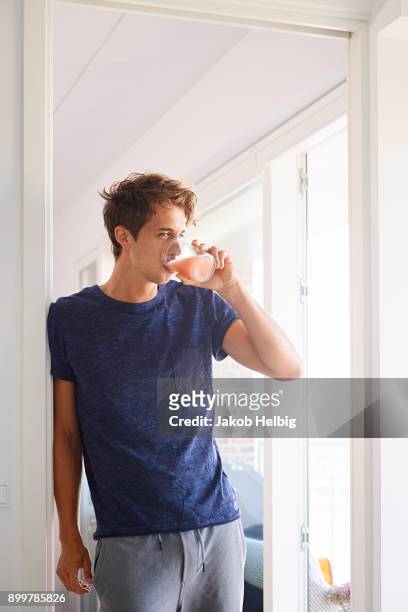 mid adult man leaning against doorway drinking fruit juice - jakob helbig stock pictures, royalty-free photos & images