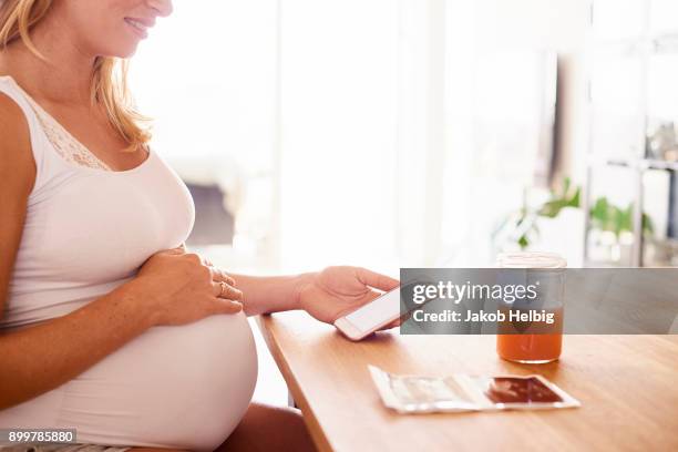 cropped shot of pregnant young woman at desk looking at smartphone and ultrasound pictures - jakob helbig stock pictures, royalty-free photos & images