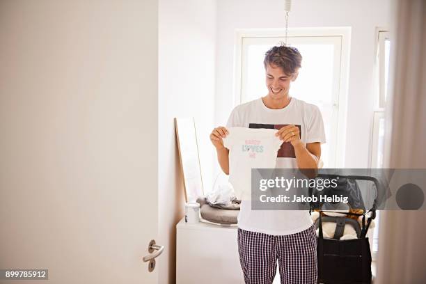 mid adult man in nursery holding baby clothes - jakob helbig fotografías e imágenes de stock