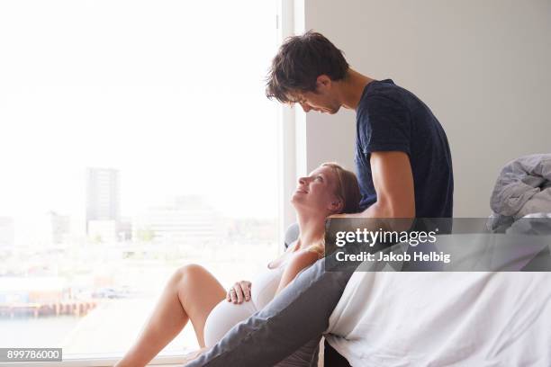 man sitting on bed gazing at pregnant girlfriend - jakob helbig fotografías e imágenes de stock