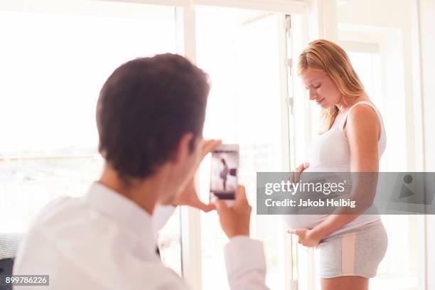 over shoulder view of man photographing pregnant girlfriend on smartphone - jakob helbig stock pictures, royalty-free photos & images