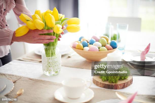 hands of woman arranging yellow tulips at easter dining table - easter flowers stock pictures, royalty-free photos & images